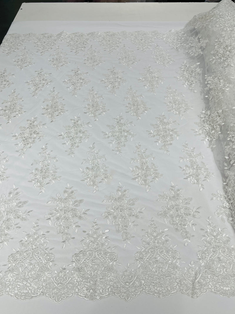 White floral design embroidery on a mesh lace with sequins and cord-sold by the yard.