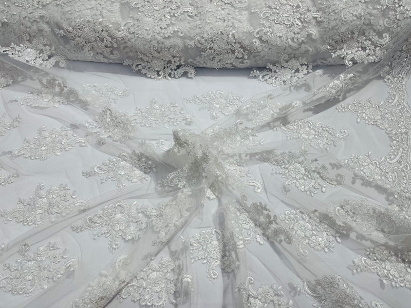 White floral design embroidery on a mesh lace with sequins and cord-sold by the yard.