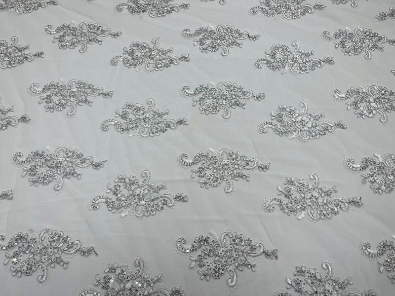 White/ silver metallic floral design embroidery on a mesh lace with sequins and cord-sold by the yard.